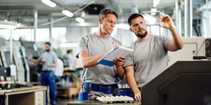 Two CNC machine operators examining finished products and taking notes at an industrial facility